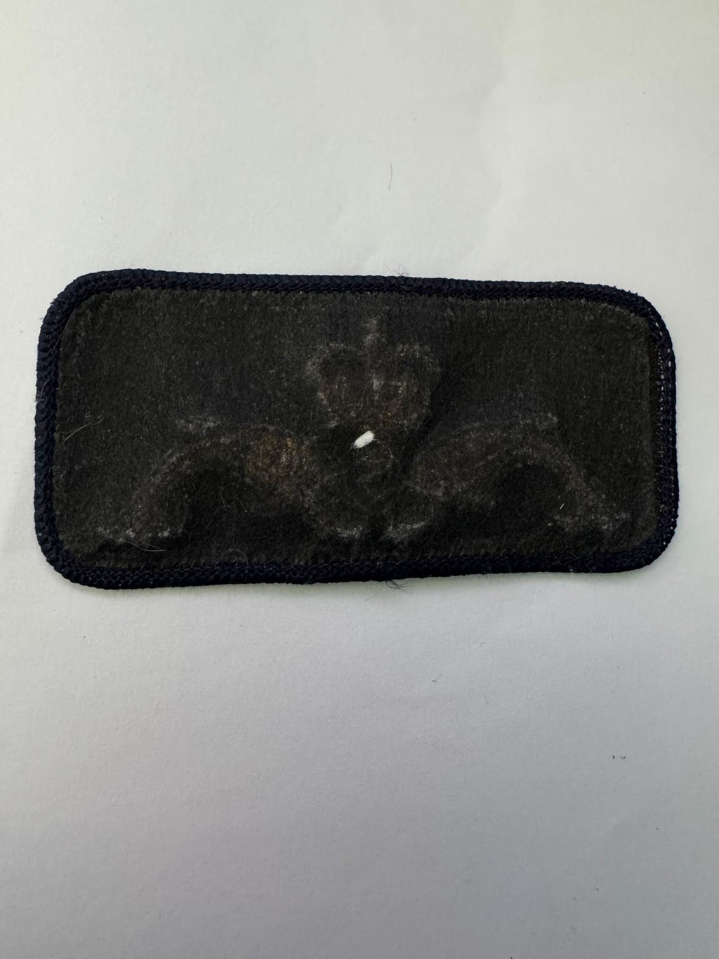 A rectangular black embroidered patch with a rounded border, featuring a dark monogram or insignia design in the center, shown on a plain light background.